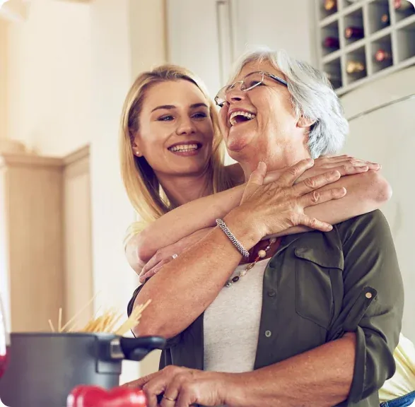 An older woman and her adult daughter hugging and smiling at home